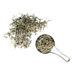 Loose Bai Hao Yin Zhen - Silver Needle White Tea leaves are scattered beside a metal measuring jug filled with more of the same tea, all set against a white background.